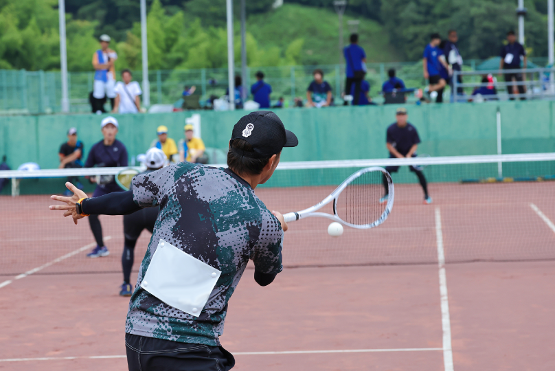 ソフトテニスの試合でボールを打ち返す選手